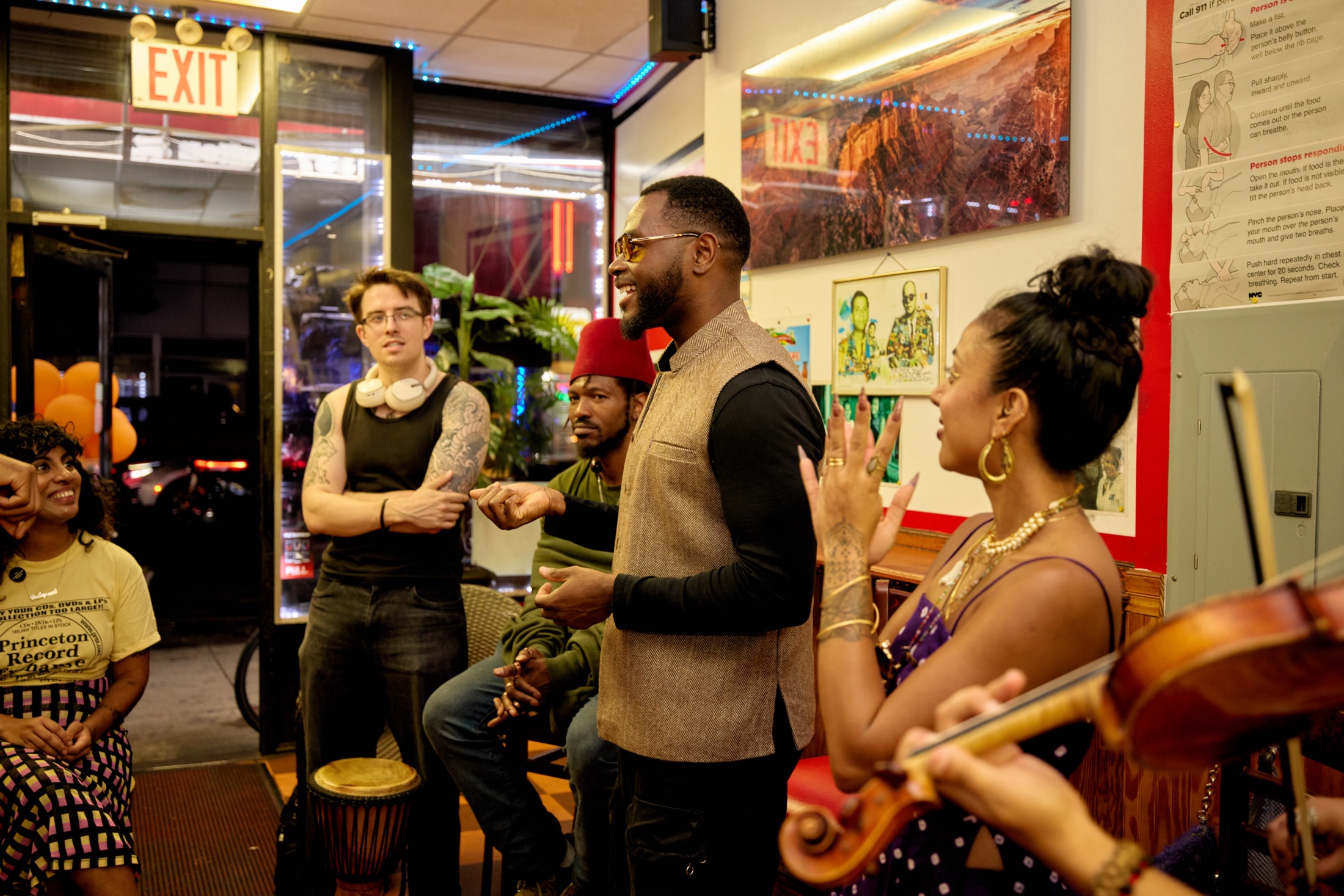 Participants gathered in a circle at a pop-up in a Brooklyn shop, laughing and trading ideas while a violinist and a drummer play.